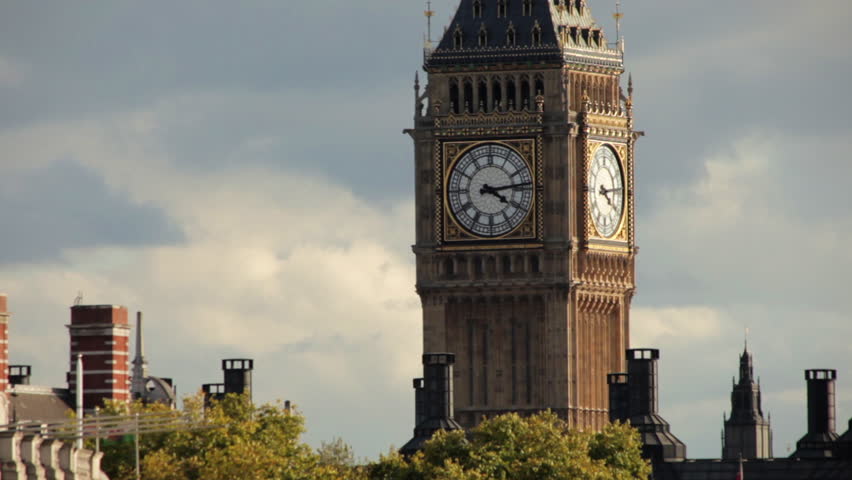 A stationary view of Big Ben clock tower in London. The dial part of it can be seen among the chimneys of surrounding houses as well as treetops. 