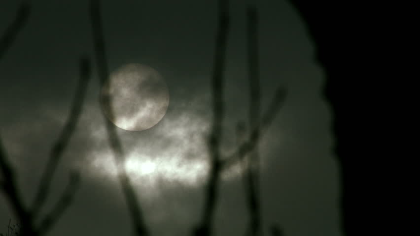 Still shot of the winter sun peeking through dark clouds.
