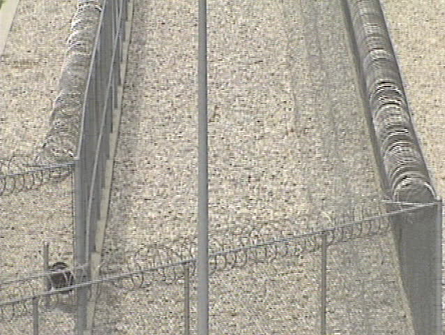 Tilt up across barbed wire to a guard tower. 
