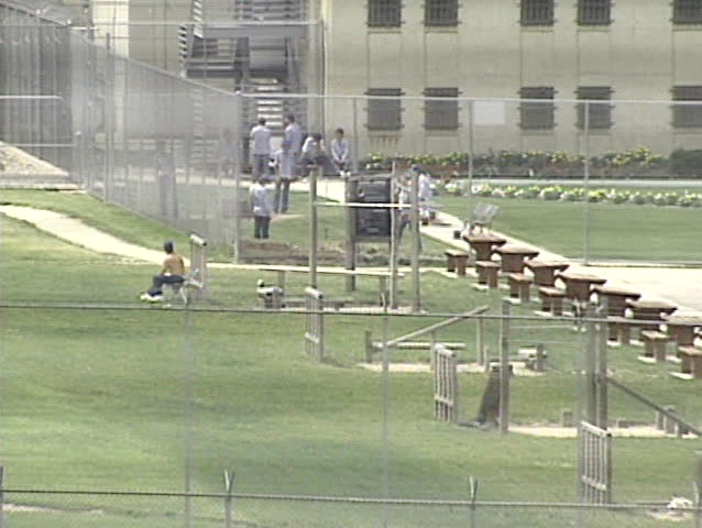 Pull from prisoners working out in an exercise yard to a wide exterior shot of a prison.