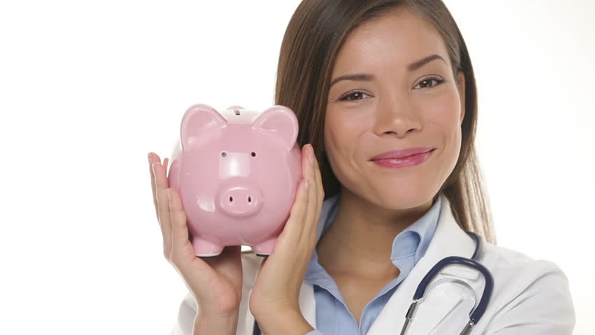 Doctor woman medical professional holding piggy bank smiling happy giving thumbs up. Health insurance or health benefits cost concept with young multicultural Asian Caucasian medical professional.