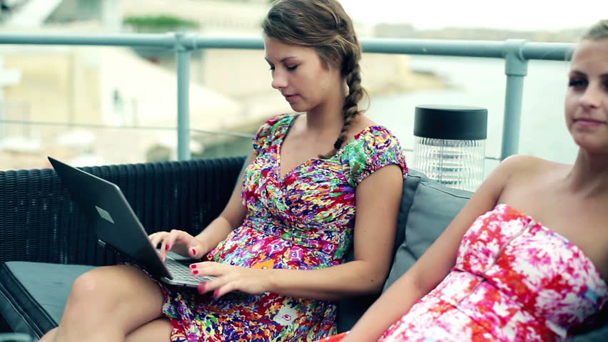 Female friends with laptop sitting in restaurant by the sea, steadycam
