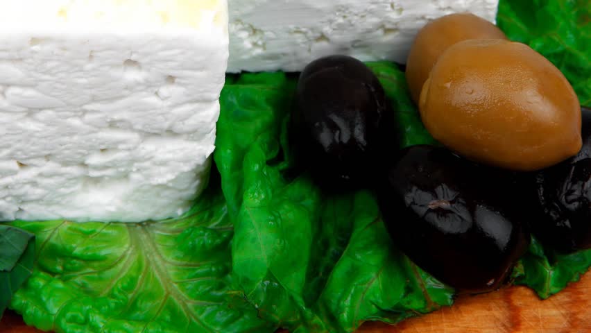 diet food : greek feta white cheese served on wooden plate with basil leaves red hot pepper black and green olives and olive oil isolated over white background