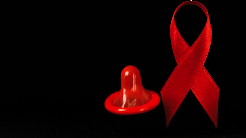 Condom dropping down in front of a red ribbon on black background in slow motion