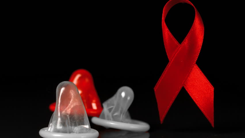 Condoms falling down in front of a red ribbon in slow motion