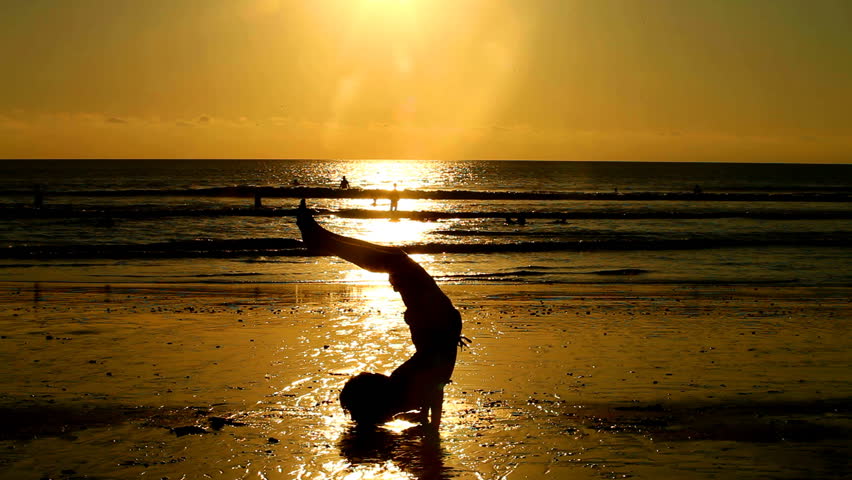 silhouetted young man doing exercises on beach at sunset in Bali