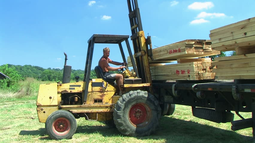 Worker operates forklift while unloading lumber on construction site. 
