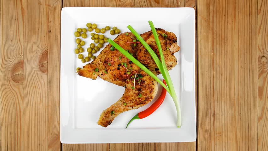 grilled meat : grilled quarter chicken garnished with green sweet peas red peppers on white plates over wooden table