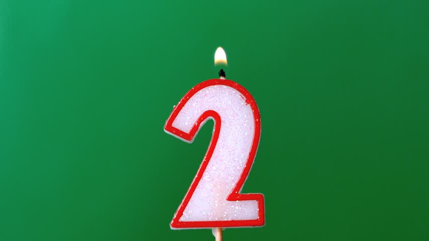 Two birthday candle flickering and extinguishing on green background in slow motion