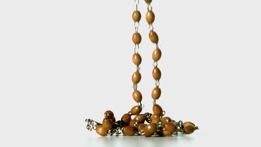 Rosary beads falling onto white surface in slow motion