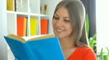 young woman reading the book then looking at camera and smiling
