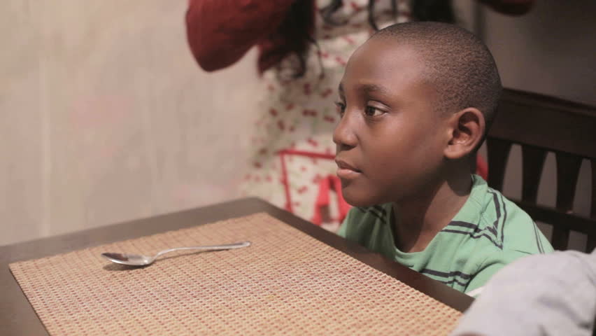 African American Black mother serving tomato soup to her son at the dinner table in the kitchen