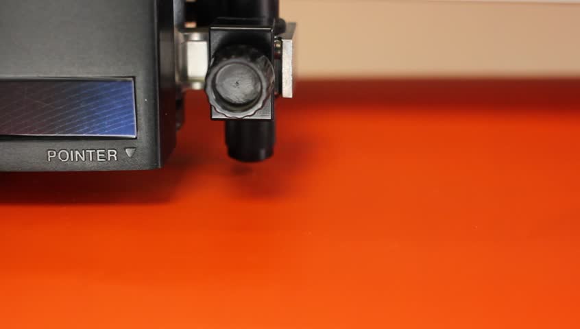 Cutting plotters use knives to cut the letters on orange vinyl film. Top view closeup
