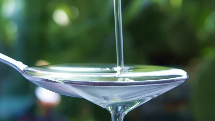 liquid (oil) flowing into the spoon on a green background