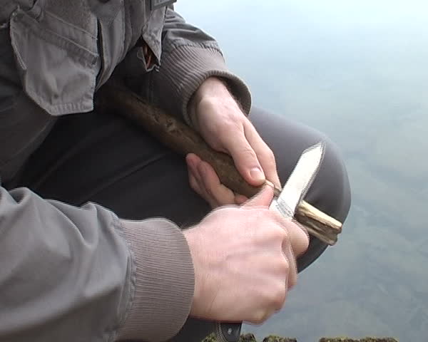 man making wooden spear with knife