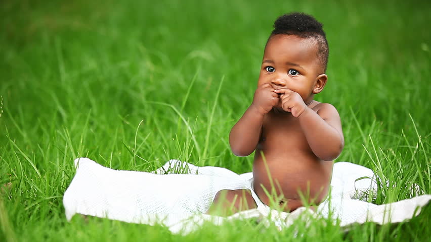 Happy little African American baby smiling while lying on blanket in garden.