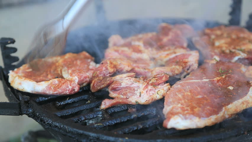 Chef cooking and arranging pork, beef and chicken steaks on barbecue grill