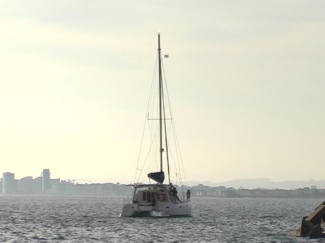 Catamaran sailing away on the ocean, after sunset into the harbor. 