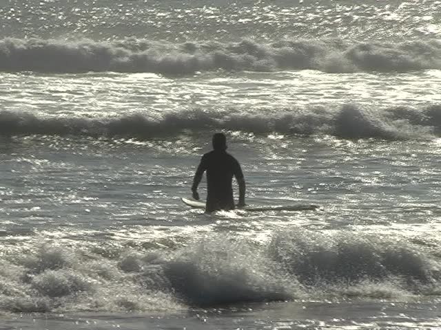 Young man running with his surfboard into the waves Ã¢â¬â silhouette against bright water 