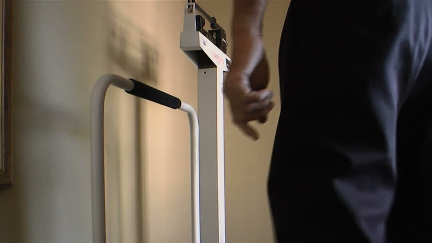 Businessman slides balancing bar on medical scale, checks weight as part of company corporate biometric health program. 1080p