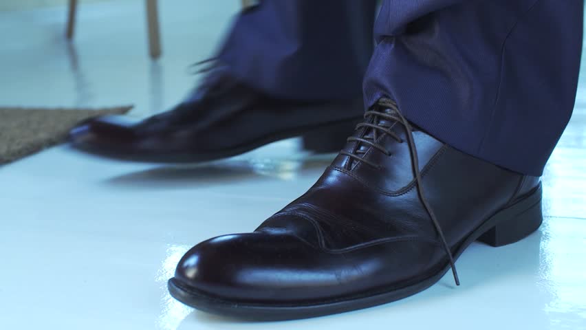 man in a suit and expensive shoes walks into frame, ties his bootlace, walks away; close-up on boots.