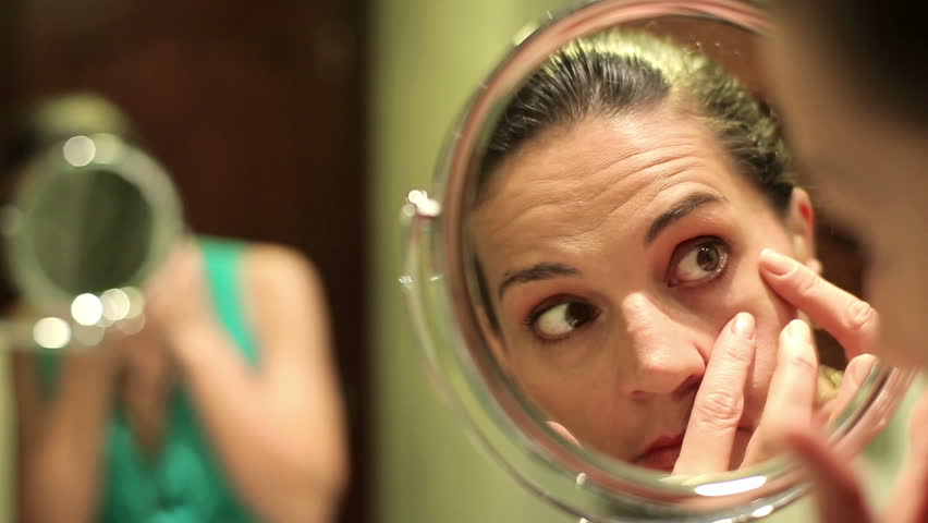 Beautiful young woman checking her face in the mirror
