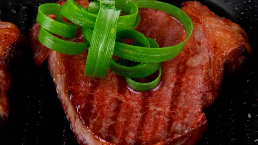 fresh grilled bloody beef steaks on black grill plate with green leaves isolated on white background
