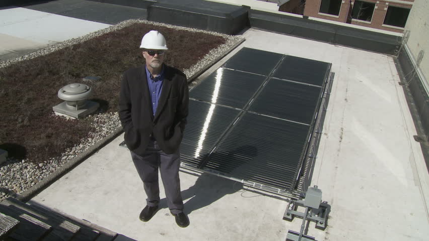 Close up of technician in front of a solar power installation. This could be a building contractor, workman, architect or site inspector, wearing sunglasses and a hard hat.
