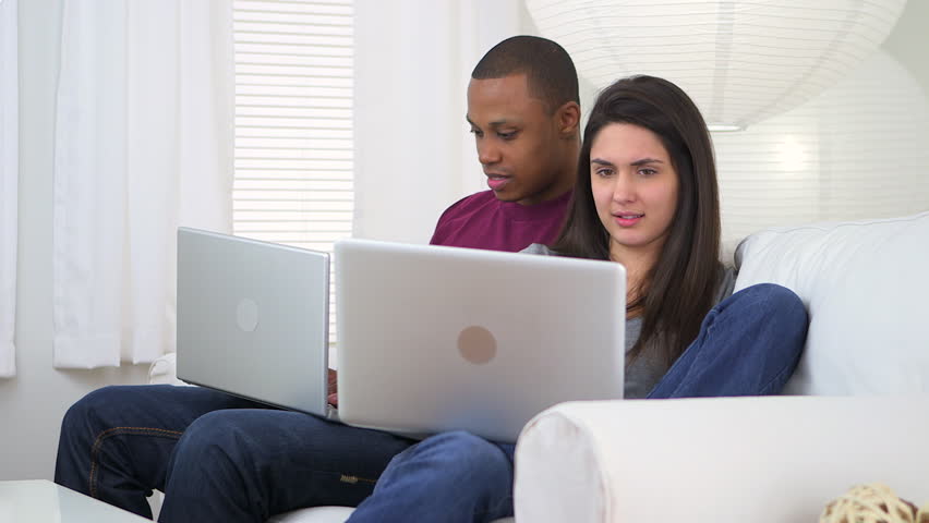 Interracial couple using notebook computers on couch