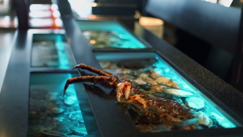 Crab sits in water with claw on edge of aquarium at restaurant