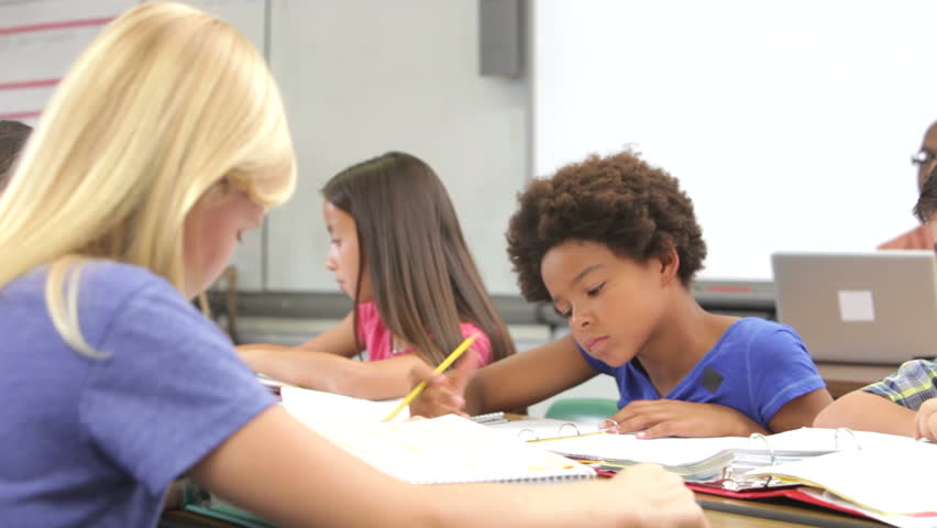 Male student working at desk raises hand to ask teacher question - teacher stand by desk and they discuss problem.Shot on Canon 5d Mk2 with a frame rate of 30fps