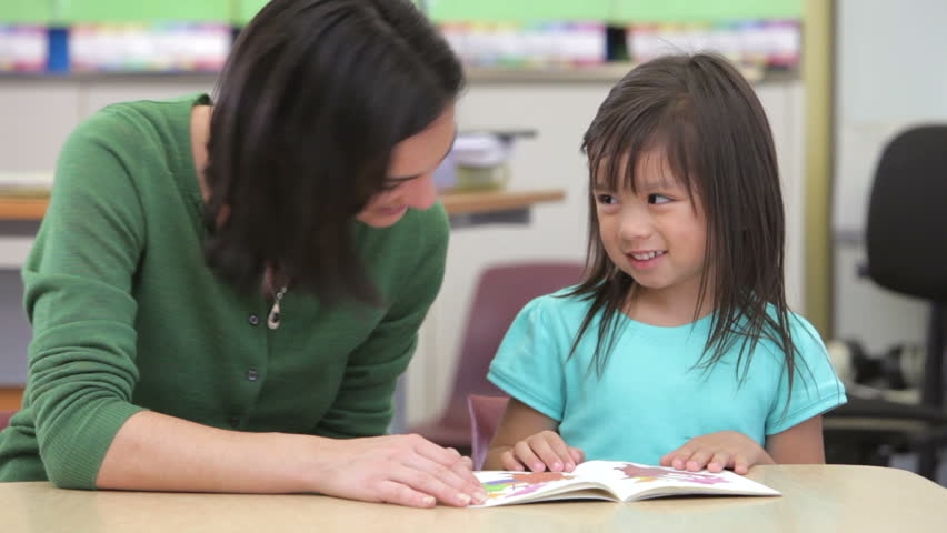 Student and teacher reading a book together in classroom at a table.Shot on Canon 5d Mk2 with a frame rate of 30fps
