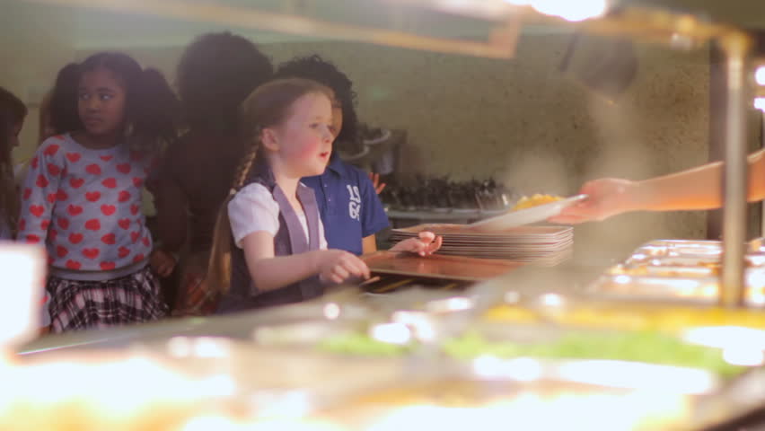 School food - a little girl in a line receiving hot steamy food from the school canteen