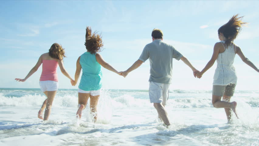Carefree young Caucasian family happily splashing ocean shallows on beach vacation shot on RED EPIC