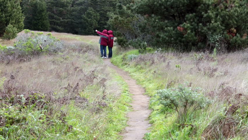 Mature couple holding hands nature trail walk. Coastal nature train northern California. Married man large gray beard. Cool weather wearing wind breaker jackets. Love after many years of marriage.