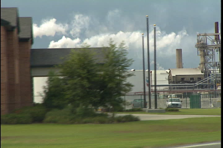 CONVENT, LOUISIANA - SEPTEMBER 4, 1999: Drive by shot past Chevron oil tank and oil refinery smokestacks spewing smoke.