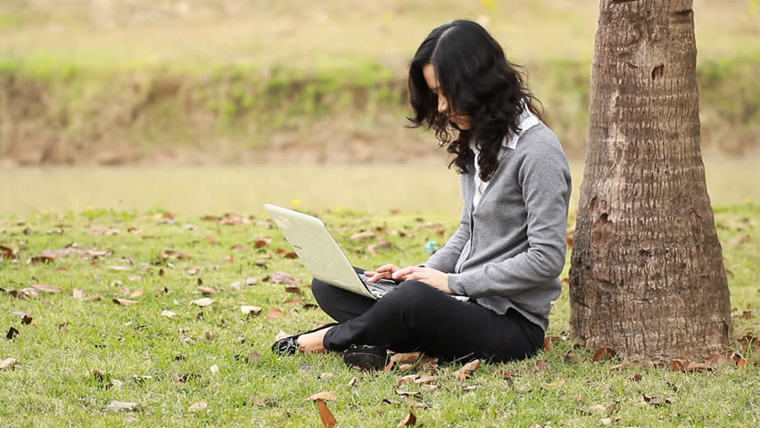 female is typing on the laptop in the park