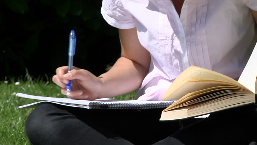 A student studying outdoors with textbook and folders