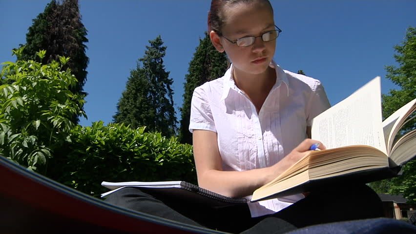 A student studying outdoors with textbook and folders