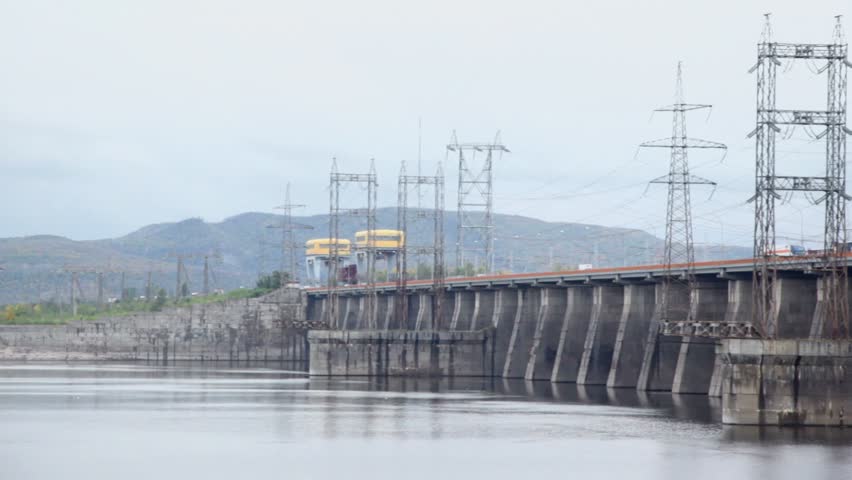Trucks ride by dam of Hydroelectric power station on river, pillars with high-voltage wires, (panoramic motion)