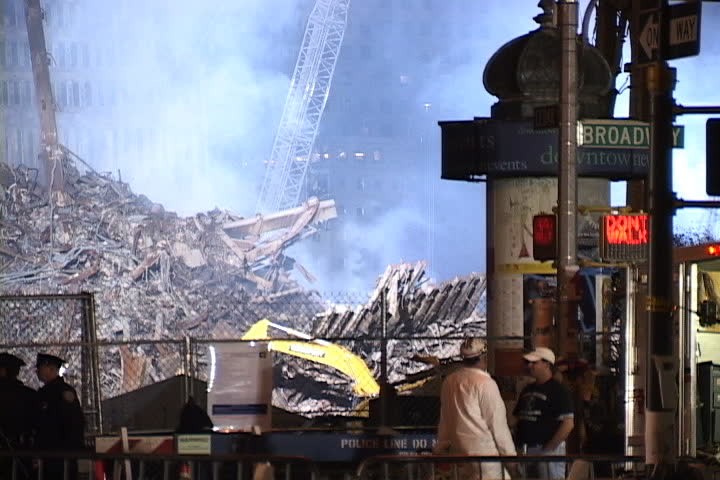 NEW YORK CITY - SEPTEMBER 28, 2001: Floodlit rubble and smoky World Trade Center remains behind fence. Emergency workers and Broadway street sign in foreground.