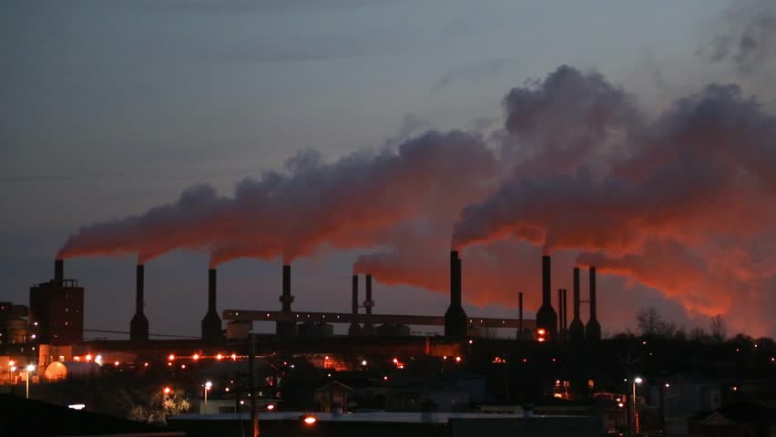 The sun sets on an Aluminum plant, giving the smoke spewing from it a bright orange glow.