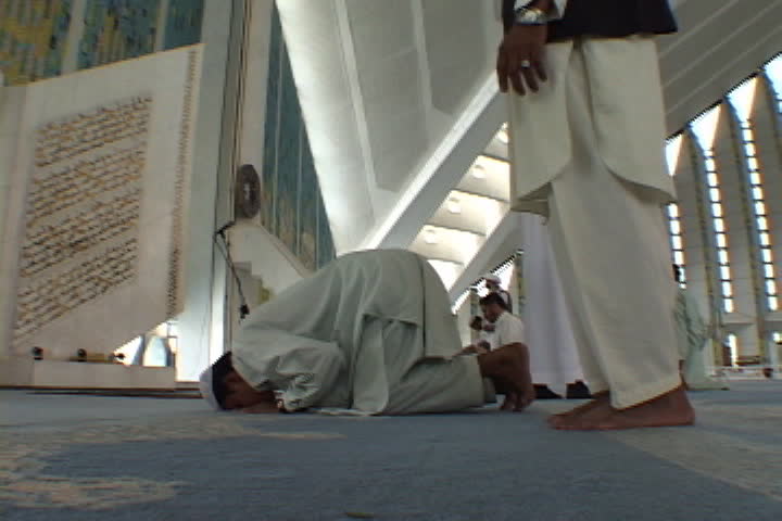 ISLAMABAD, PAKISTAN - NOVEMBER 01, 2001: Two men kneel and pray in front of large scale replica of Koran.