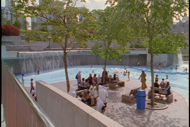 KUALA LUMPUR - OCTOBER 22, 1999: Petronas plaza and towers; WS plaza with waterfalls on exterior wall, pan right across kids playing in shallow pool.