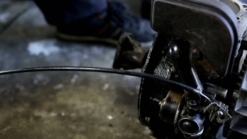 Young man cleaning a dirty engine of a mini motor. A lot of oil. Working in workshop on the floor. Unscrewing parts of the motor.