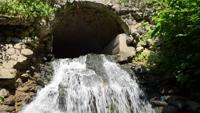 stream brook water cascade flow run through old retro stone arch.