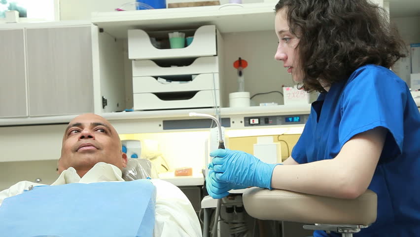 A young intern talks to a patient sitting in the dental chair as they wait for the dentist to enter.