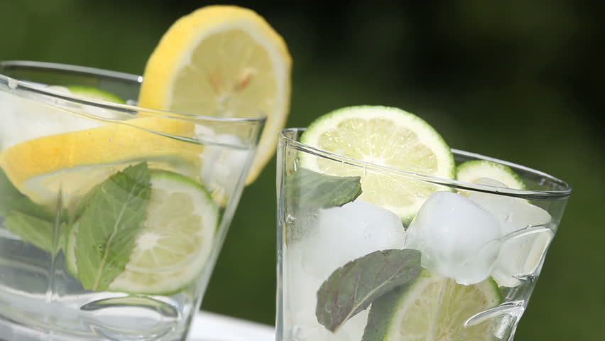 Glass with ice cubes, mint, lemon and lime and jug with pouring lemonade.
