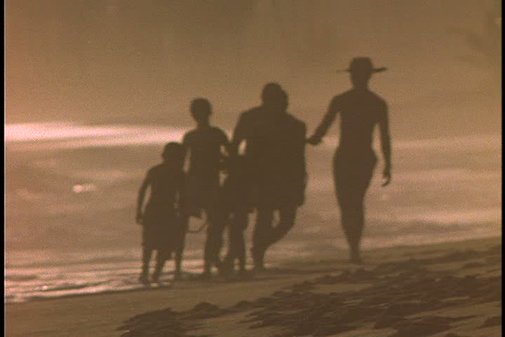 Slavery reenactment in Ghana, Africa. MS silhouette of overseer leading five men in chains (two are boys) up beach in very bright sunlight. 
