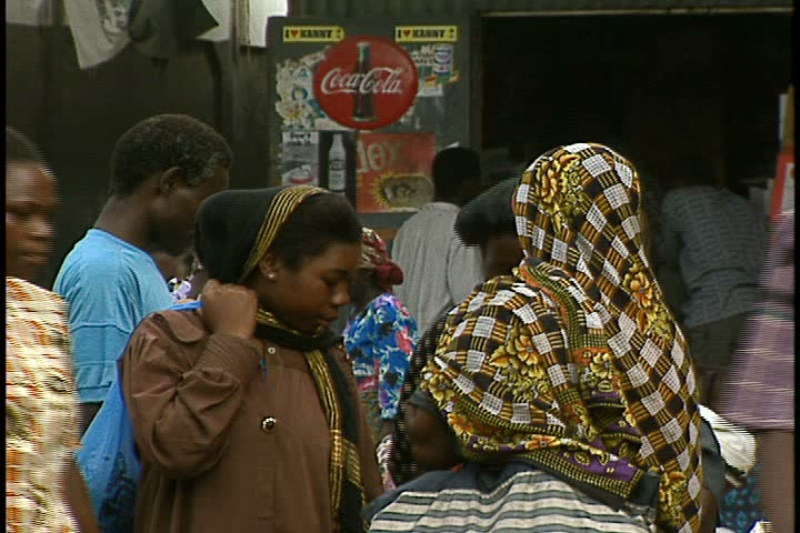MOMBASA, KENYA, AFRICA - DECEMBER 01, 1998: Mombasa outdoor market; women in colorful head scarves, pedestrians and traffic pass by camera in bustling marketplace.